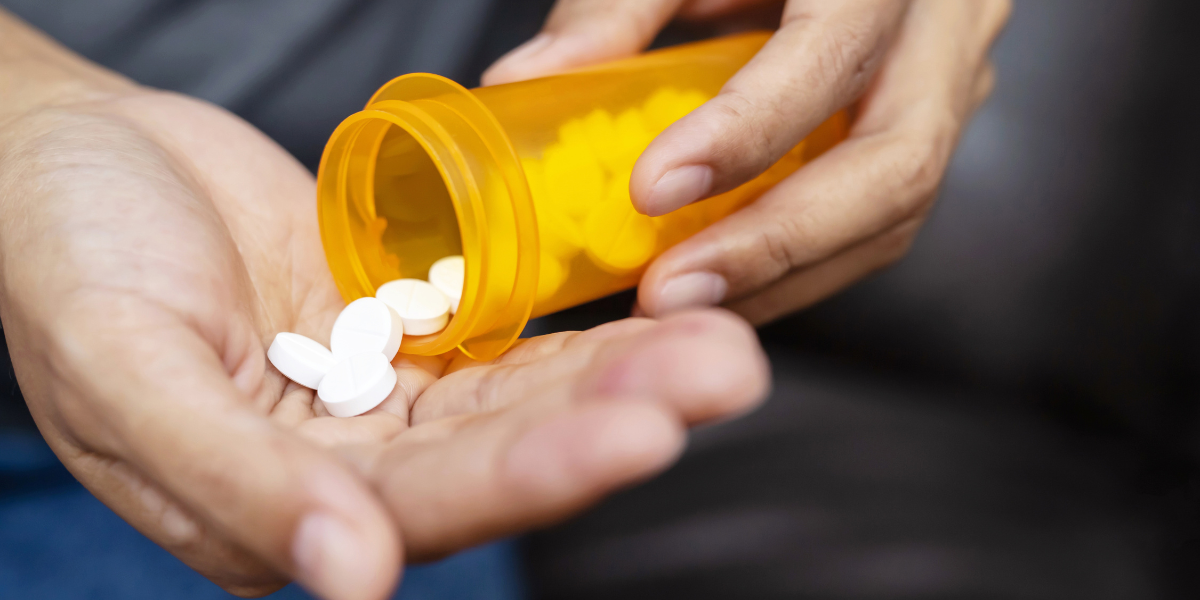 Hands holding white pills beside an open orange prescription medicine bottle.